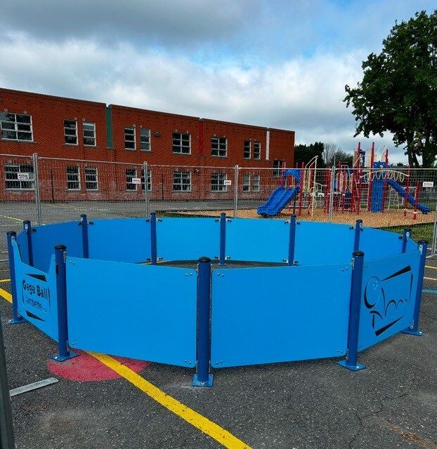 Une clôture bleue entoure une aire de jeux avec un bâtiment en briques en arrière-plan