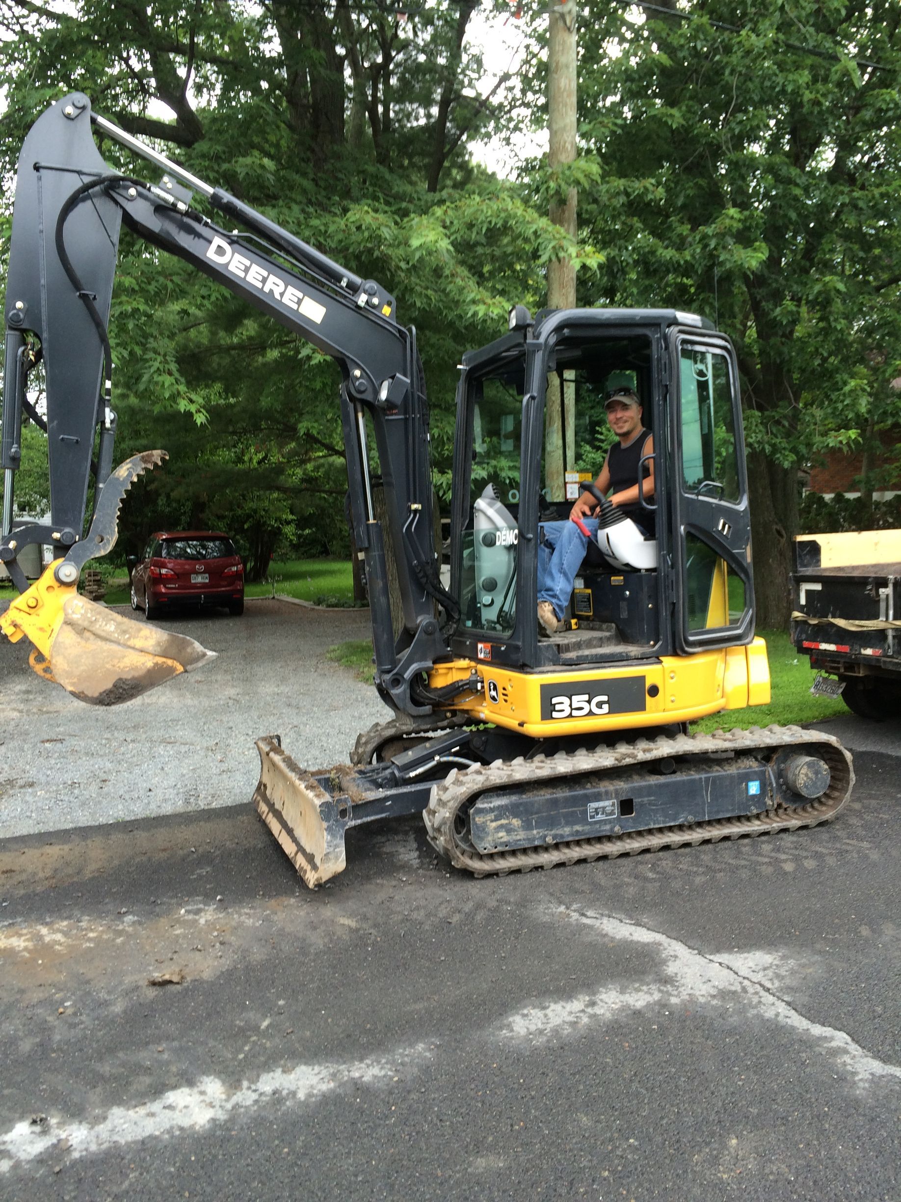 Un homme conduit une petite excavatrice sur un parking.