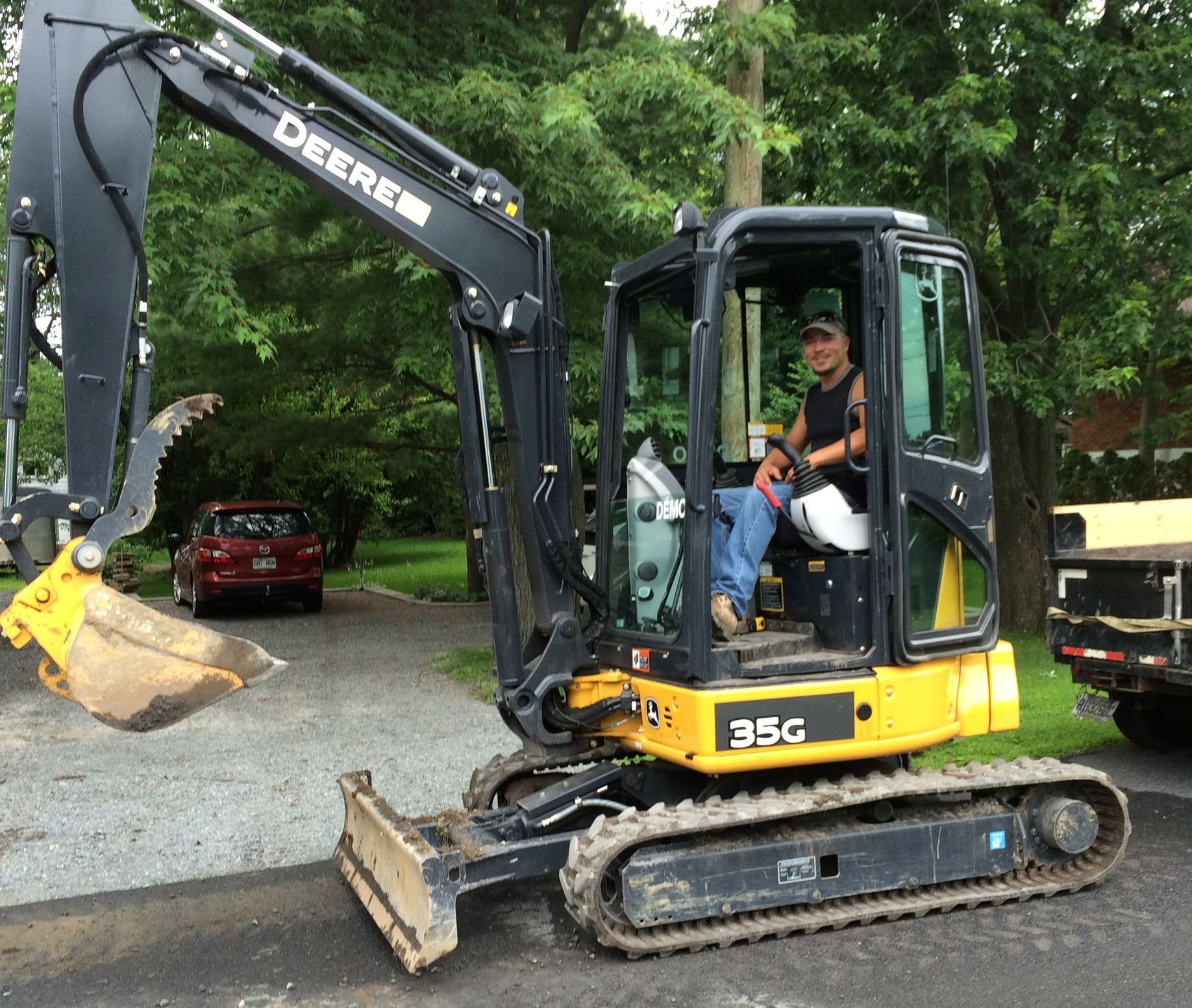 Un homme conduit une excavatrice Deere dans une allée