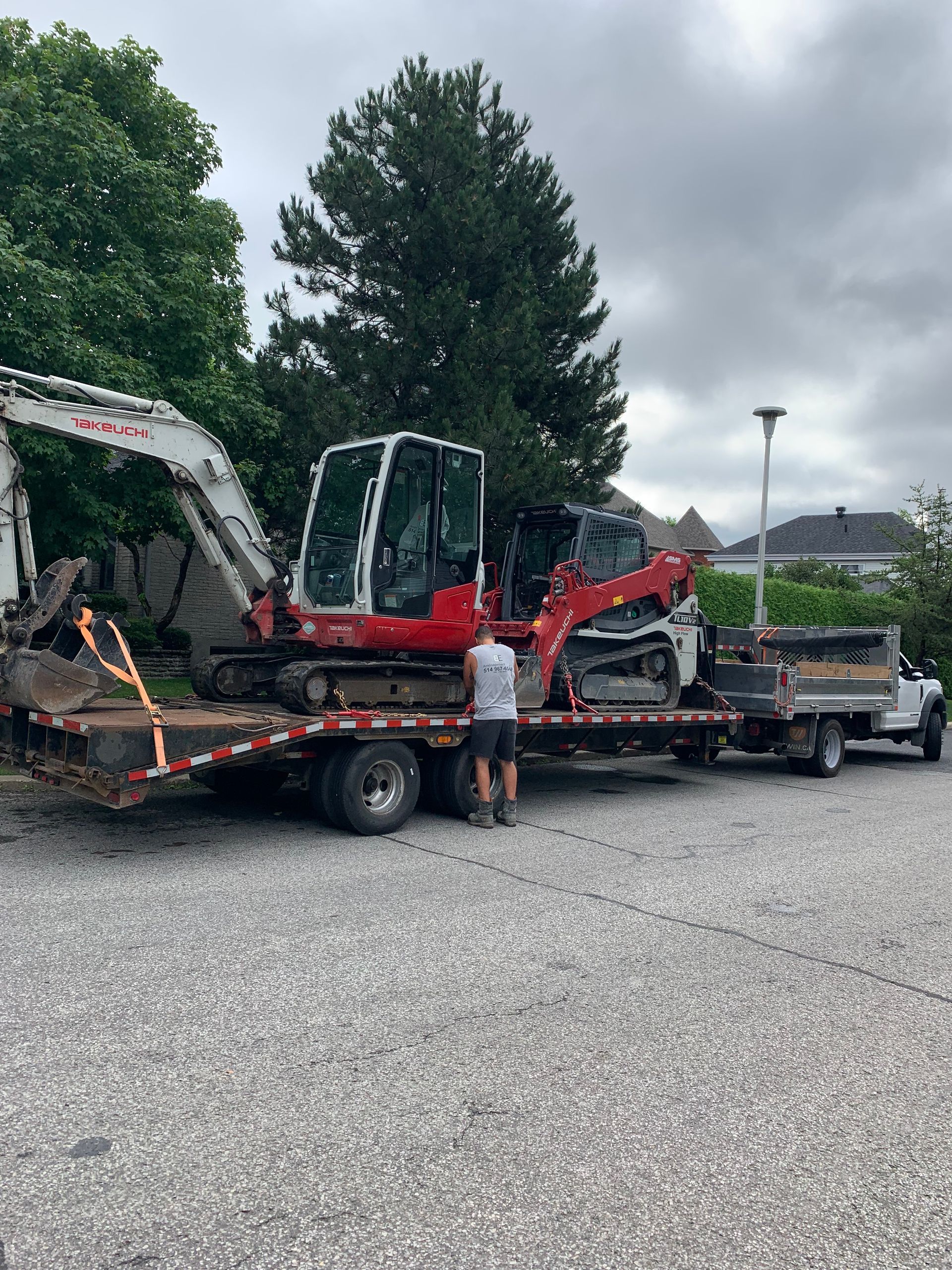 Un homme se tient à côté d'une dépanneuse avec deux excavatrices dessus.