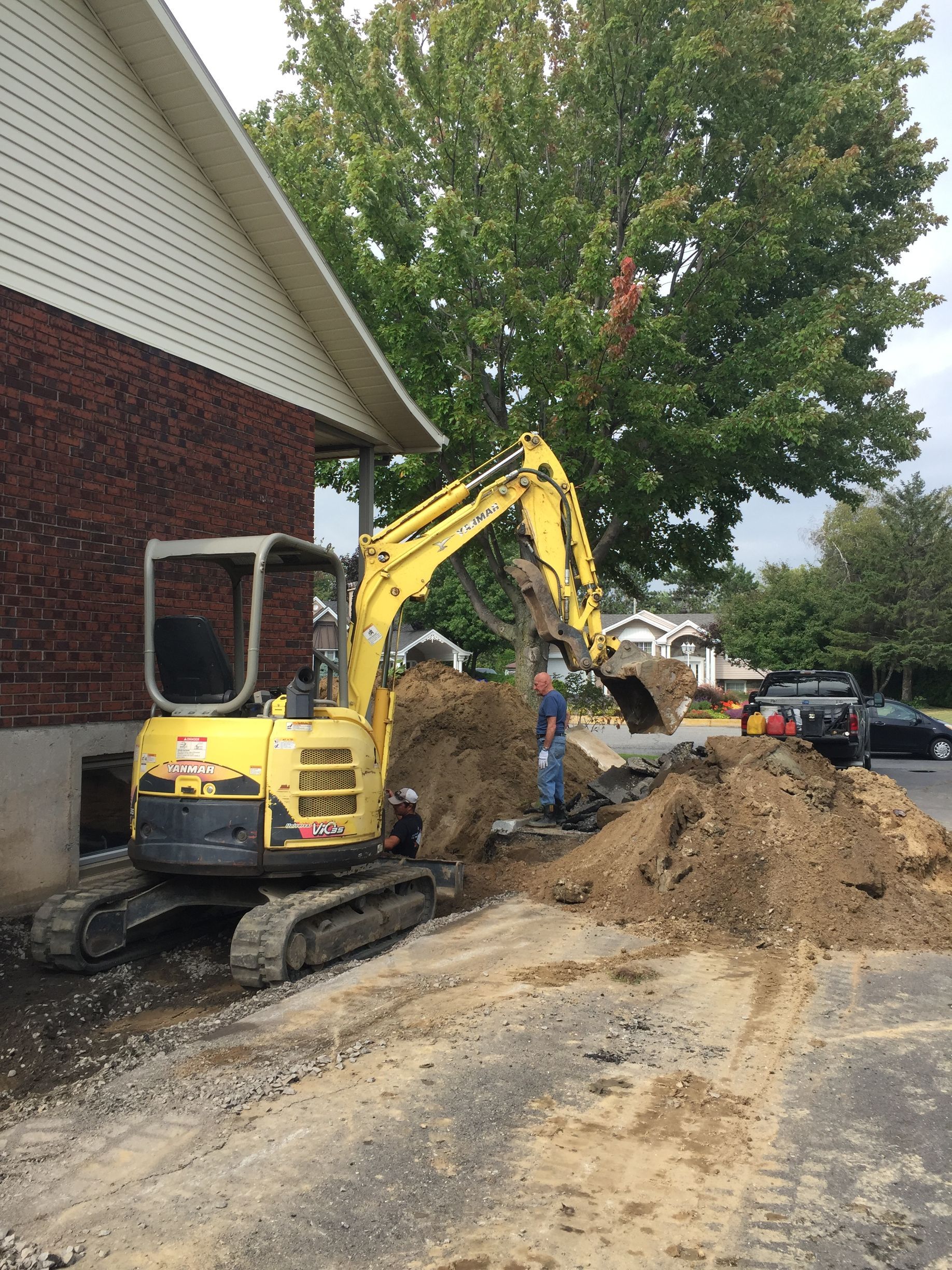 Une excavatrice jaune creuse un trou devant une maison.
