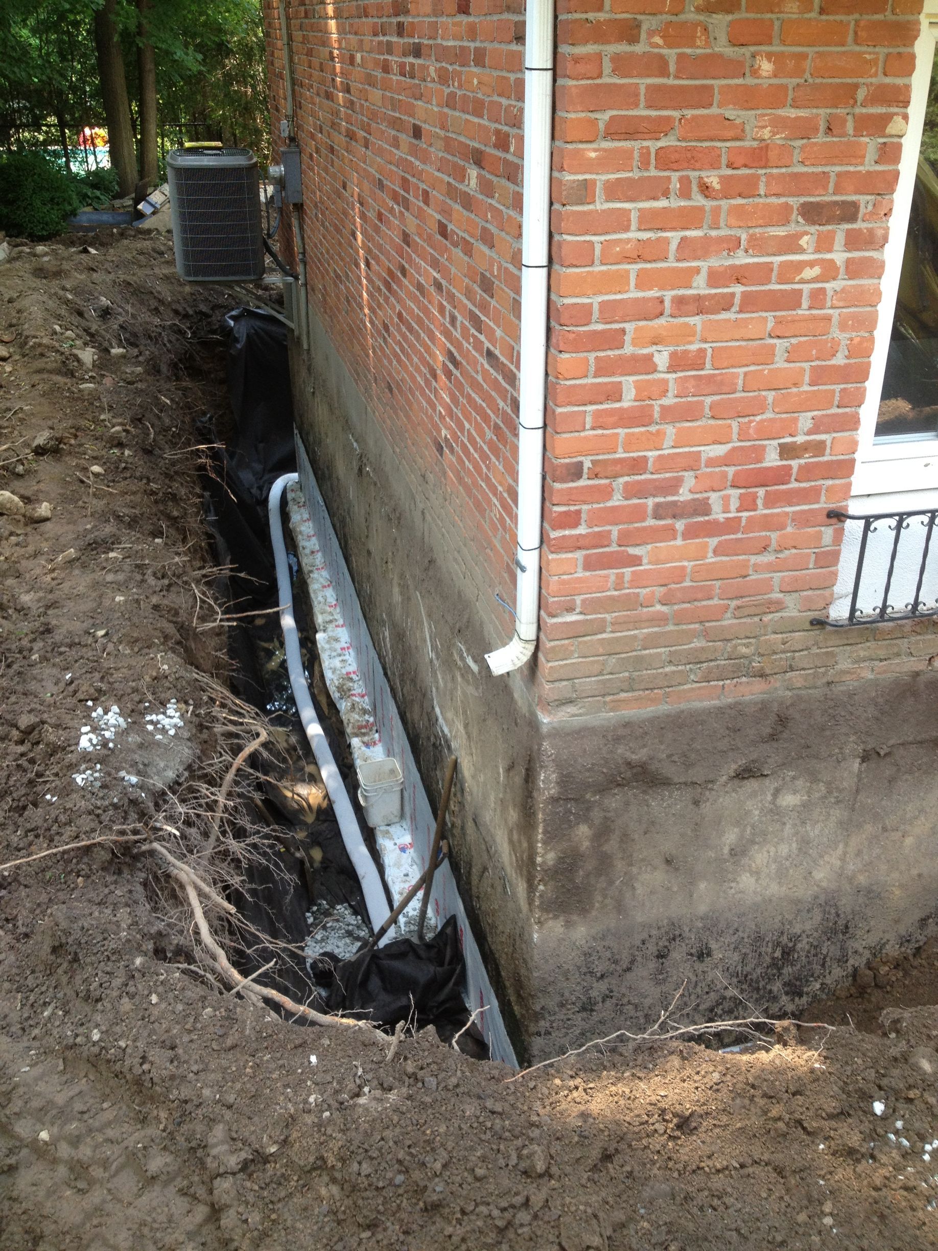 Un système de drainage est en cours d'installation sur le côté d'un bâtiment en briques.