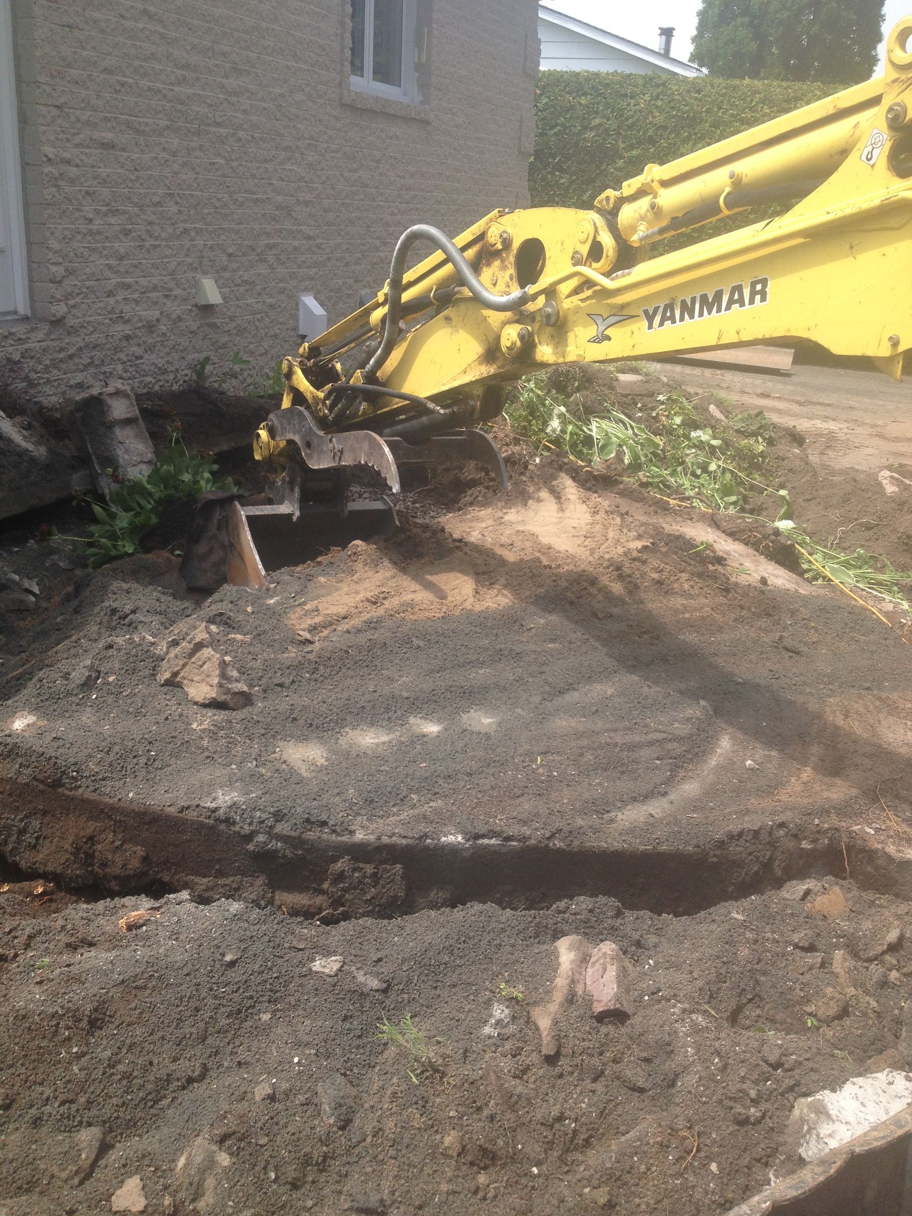 Une excavatrice jaune creuse un trou dans la terre devant une maison.
