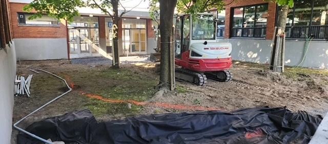 Une petite excavatrice creuse un trou dans la terre devant un bâtiment.