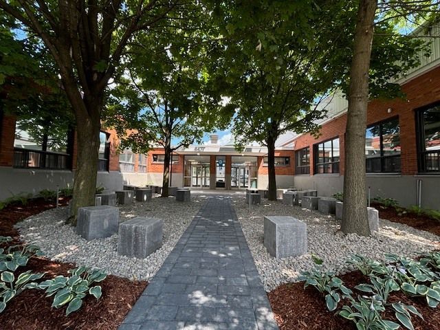 Un bâtiment en briques avec une passerelle entourée d'arbres et de bancs