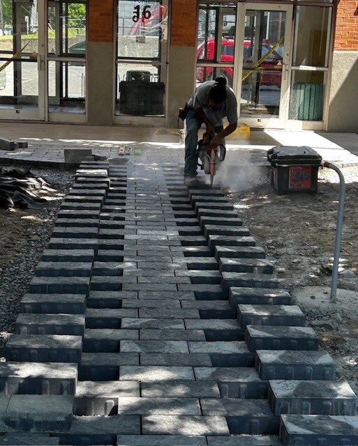 Un homme coupe des briques avec une scie devant un bâtiment portant le numéro 16