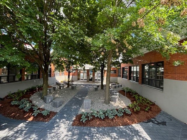 Une cour avec des arbres et des bancs devant un bâtiment en briques.