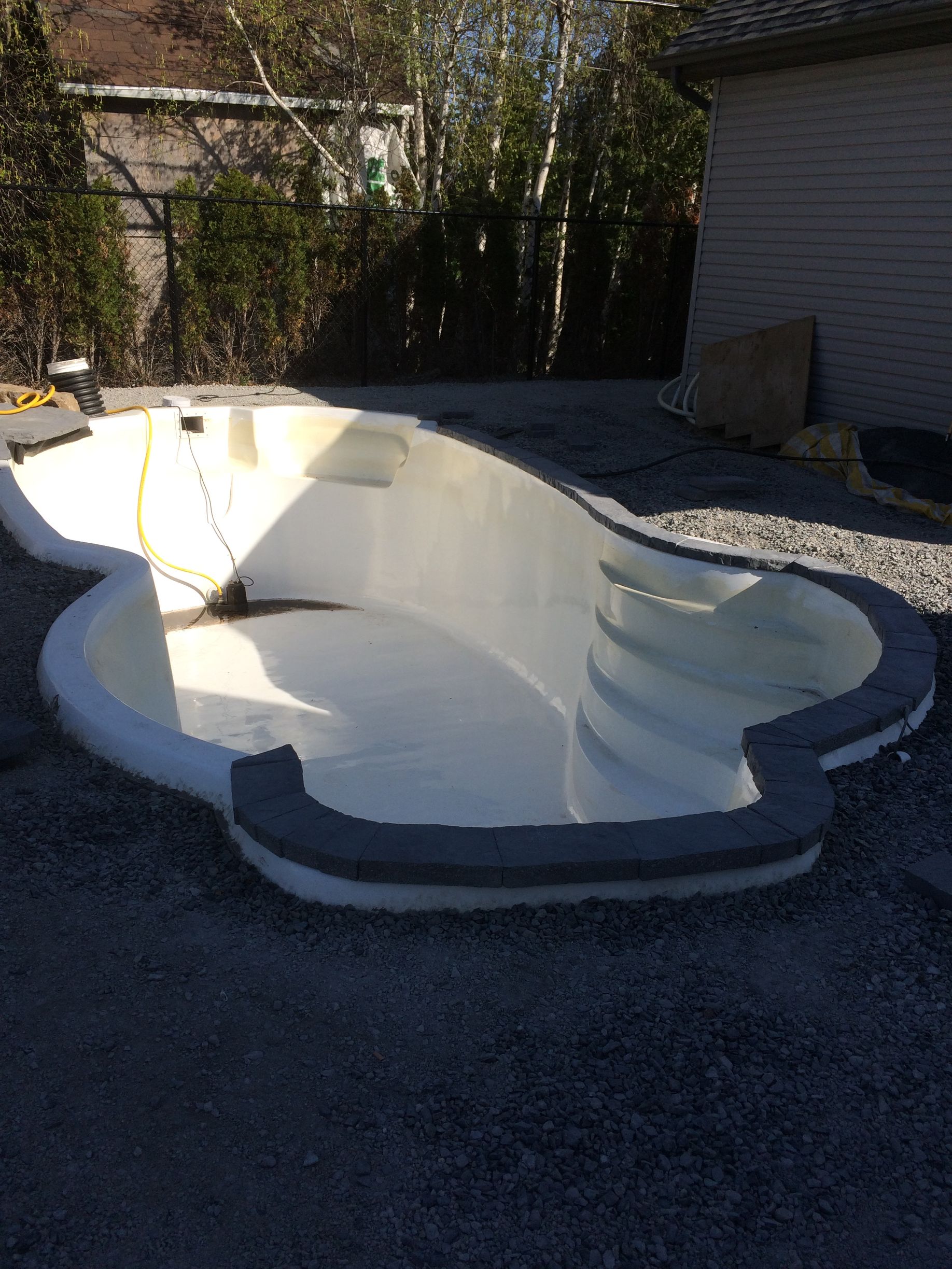 Une grande piscine blanche est posée sur un terrain en gravier.