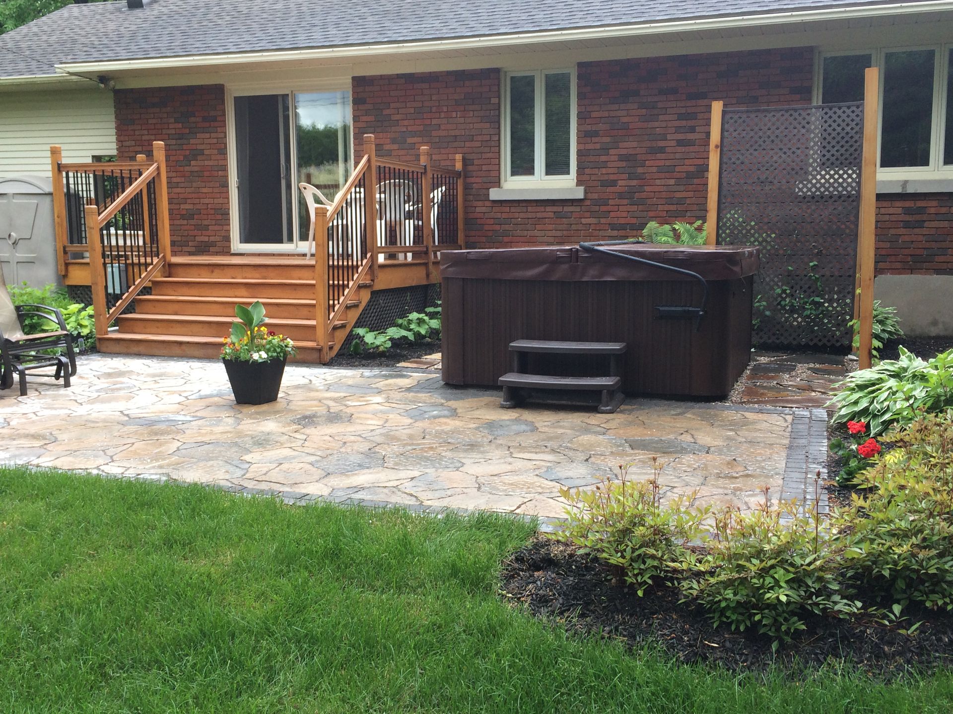 Un bain à remous est installé sur une terrasse devant une maison en briques.