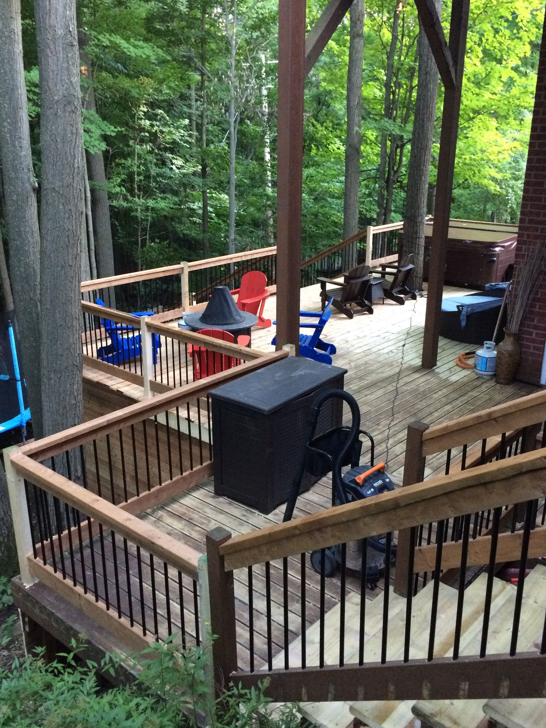 Une terrasse en bois avec des chaises et un trampoline dans les bois