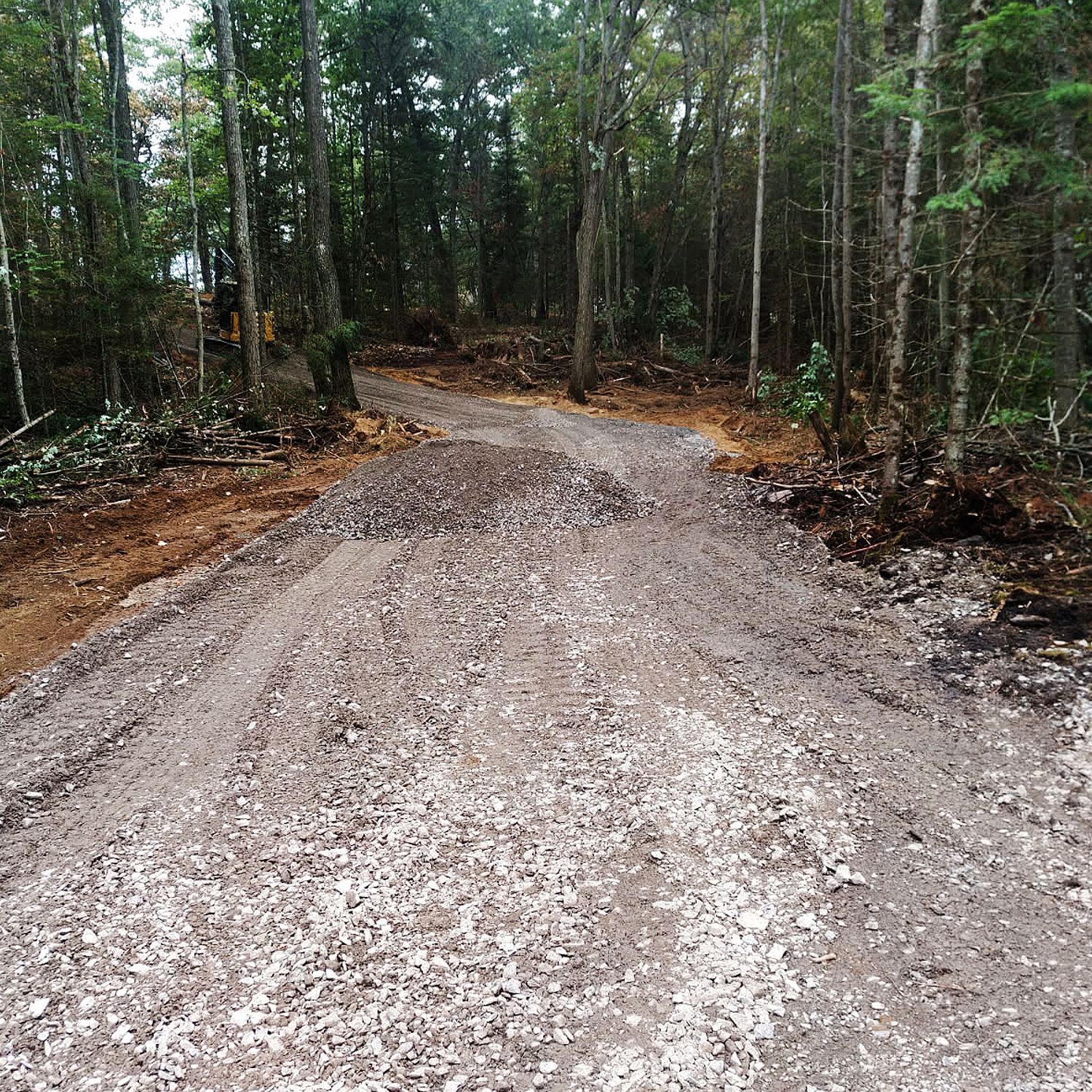 A newly graveled path cuts through a wooded area, with piles of loose dirt and gravel visible along the edges.