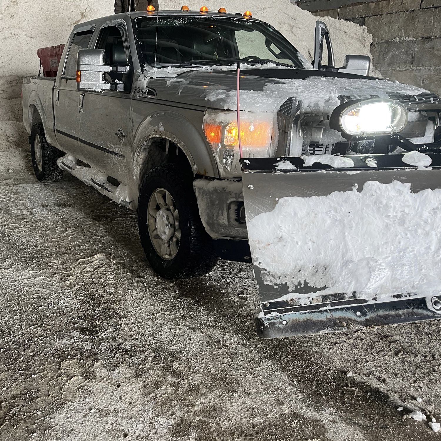 A silver pickup truck equipped with a snow plow, parked in a snow-covered storage area.