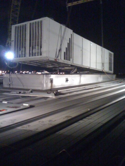 A large white box is being lifted by a crane at night