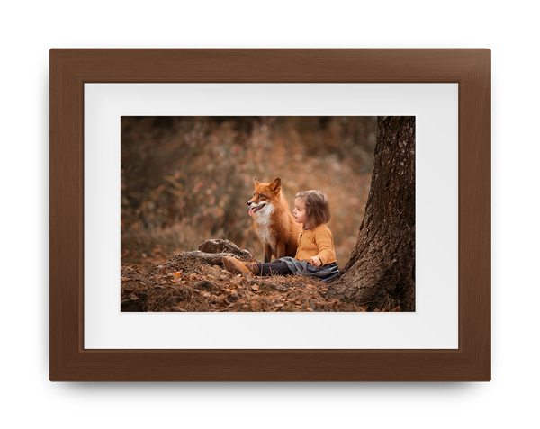 A little boy is laying under a tree with a fox.