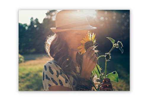 A woman in a hat is smelling a sunflower in a field.