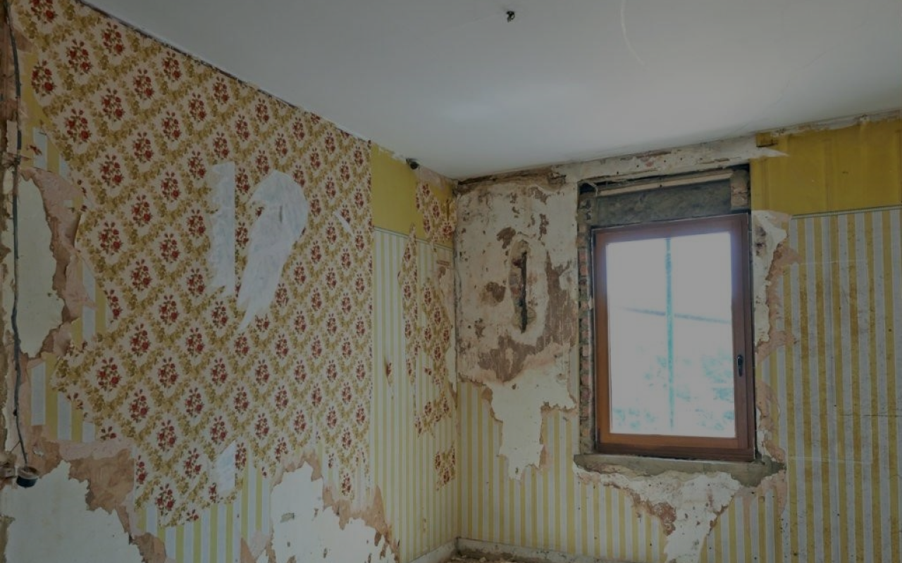 A room with peeling wallpaper and a window.