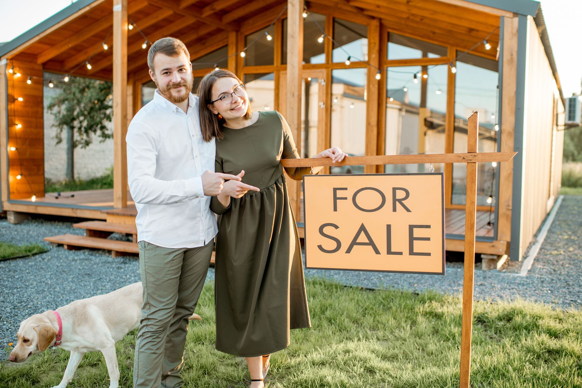 A man and woman are standing next to a for sale sign in front of a house.