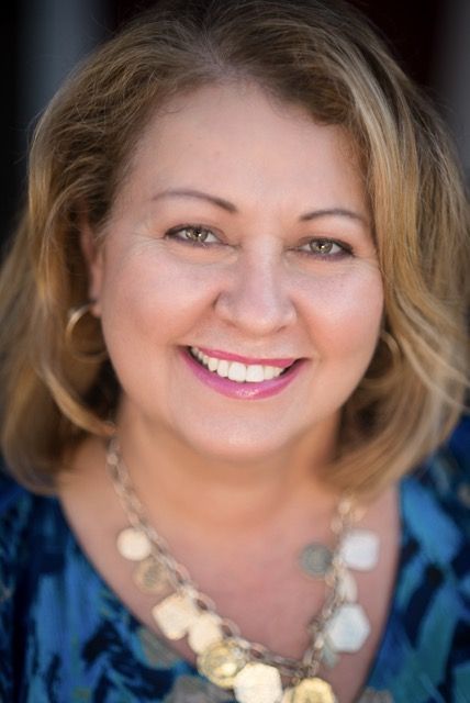 A woman wearing a blue shirt and a gold necklace is smiling for the camera.