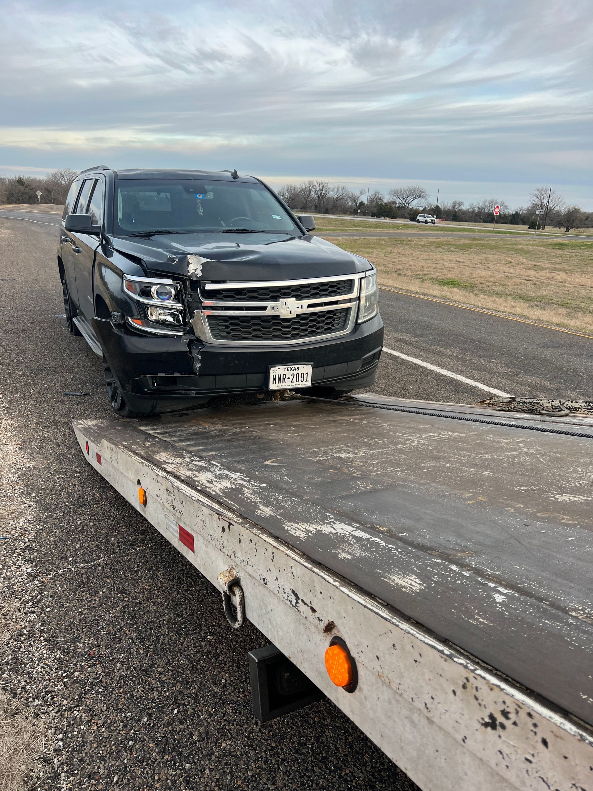 A black suv is sitting on top of a tow truck on the side of the road.