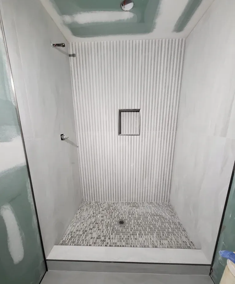 Newly tiled shower with gray walls and a vertical, ribbed accent wall; pebble tile floor.