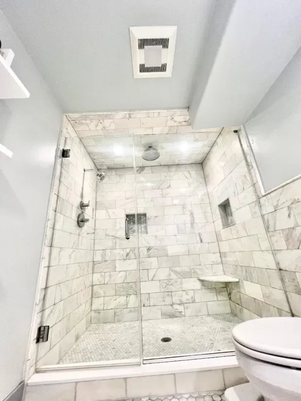 Bathroom shower with marble tile, glass door, and a built-in bench. A toilet is in the foreground.