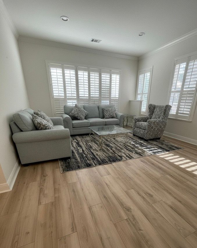Living room with light blue furniture, shutters, and wood flooring. A patterned rug is in the center.
