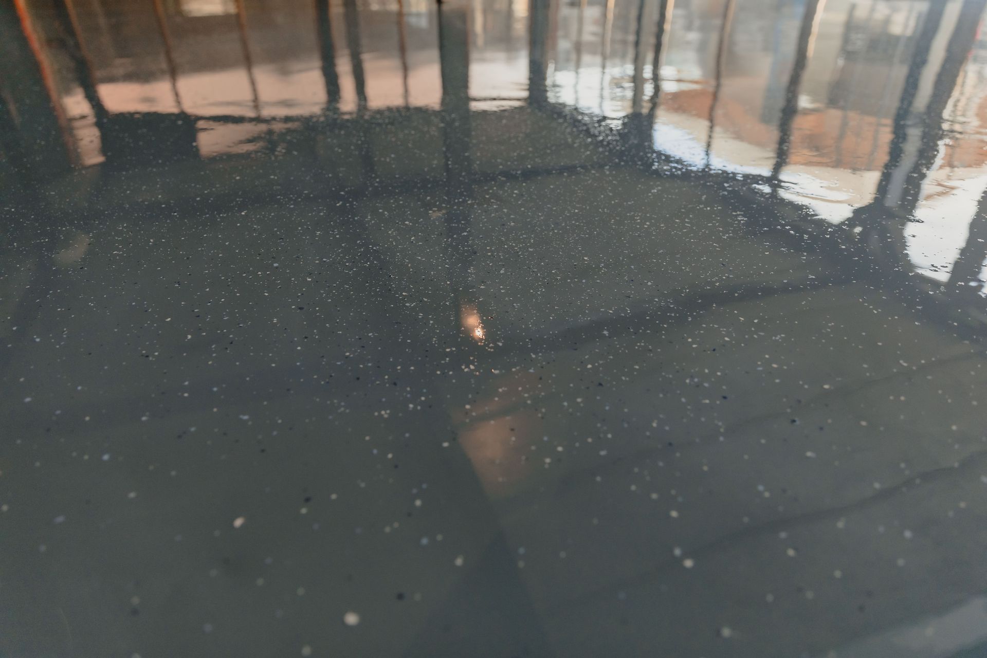 Dark, speckled surface reflecting a building with sunny light and a small, bright object.