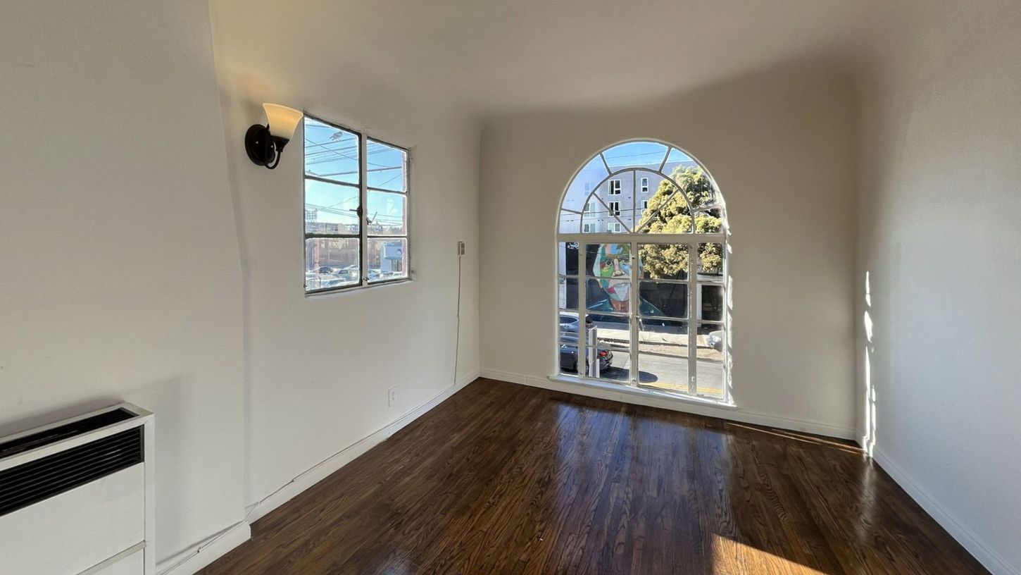 Empty room with arched window, dark wood floors, white walls, and a small rectangular window.