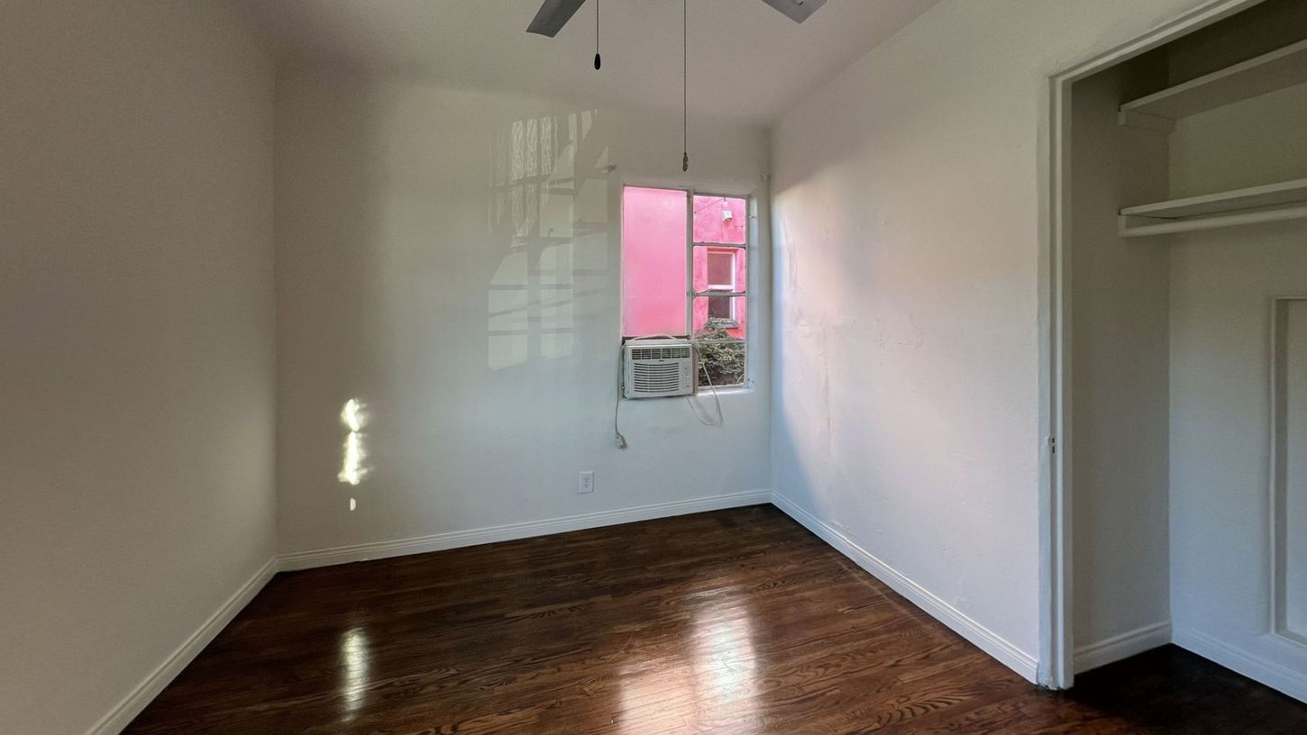 Empty room with wooden floor, window with pink exterior visible, and closet.