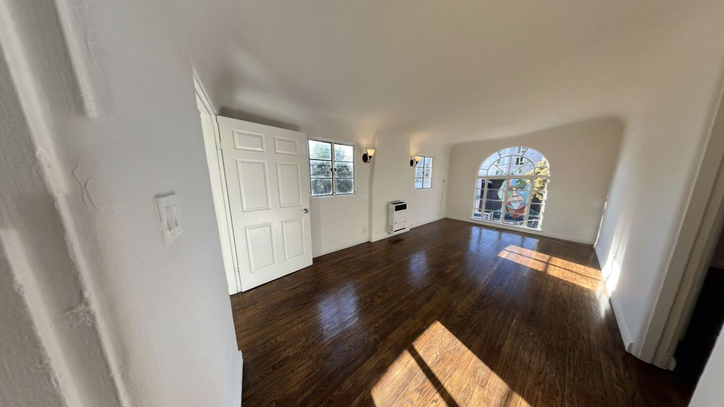 Bright, empty room with dark hardwood floors, white walls, and an arched window.