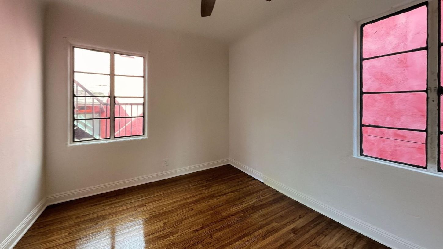 Empty room with wood floors and two windows; one with pink glass.