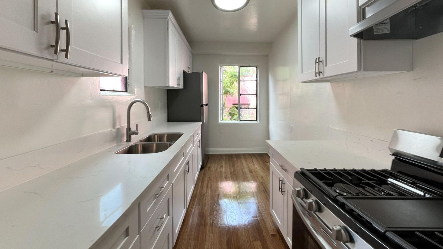 Bright, galley kitchen with white cabinets, stainless steel appliances, and a window.