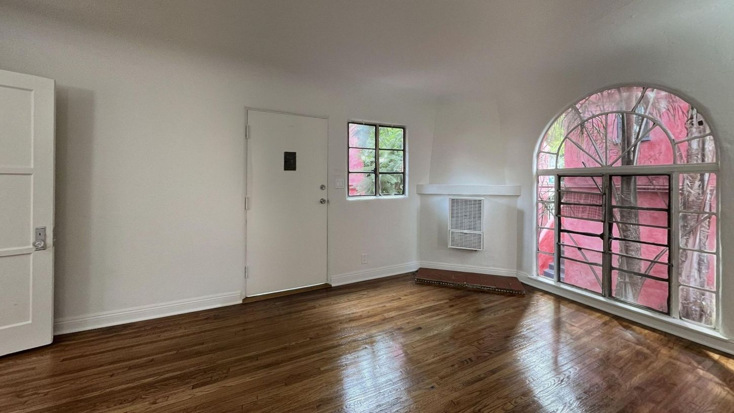 Room with wood floor, white walls, and large arched window with red frame.