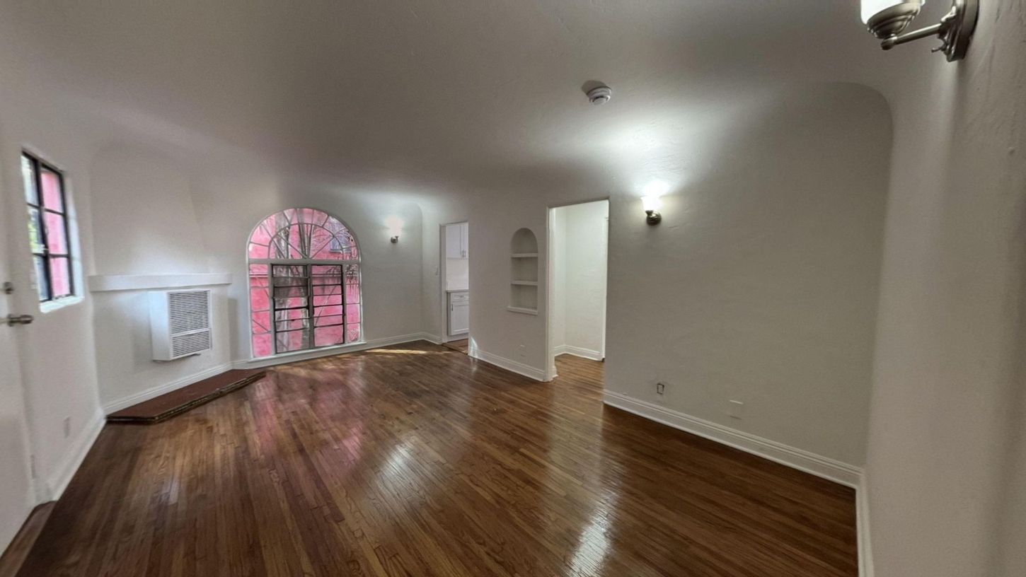 Empty room with arched doorway, hardwood floors, and white walls.