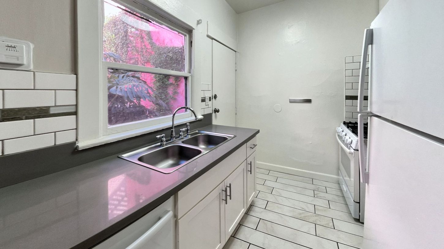 Kitchen with white cabinets, stainless steel sink, window, and white appliances.