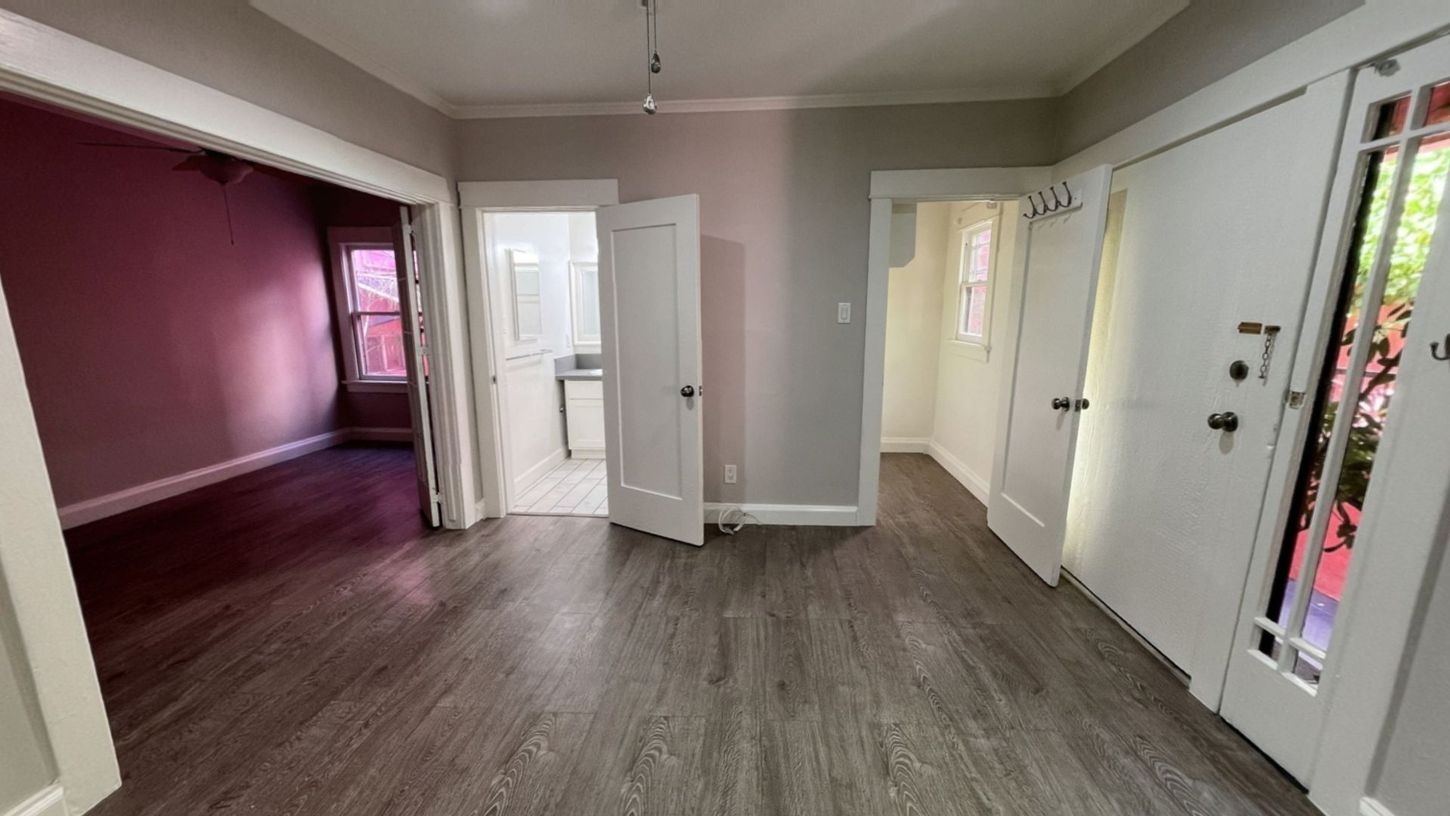 Interior view of a home with open doorways to different rooms; hardwood floors, white doors, and painted walls.