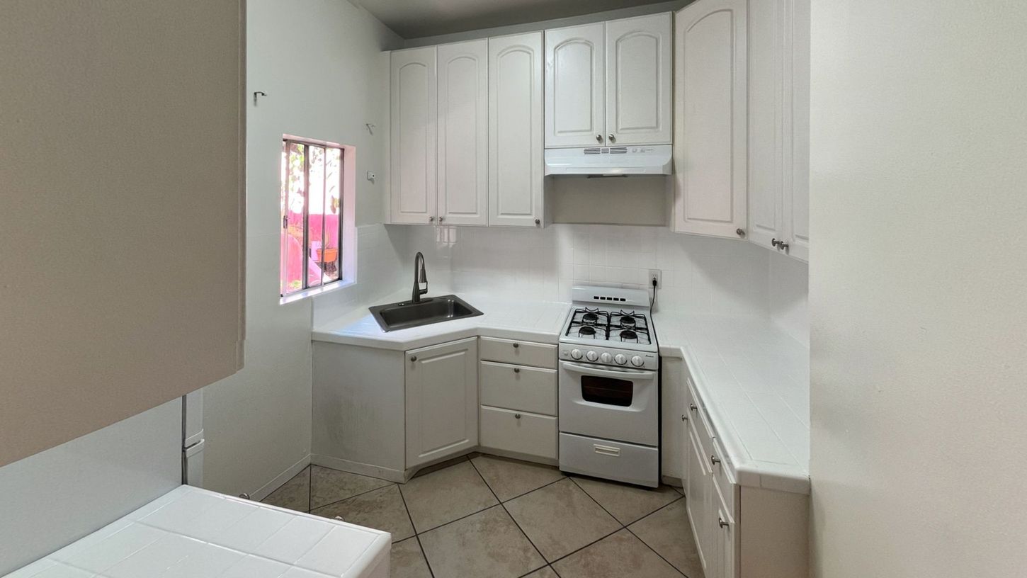 Small white kitchen with cabinets, stove, sink, and a small window.