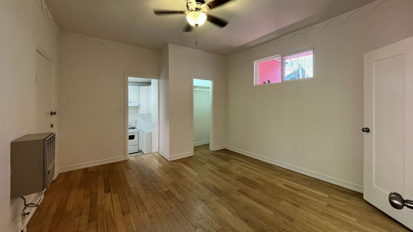 Empty room with hardwood floors, a ceiling fan, and access to a kitchen and bathroom.