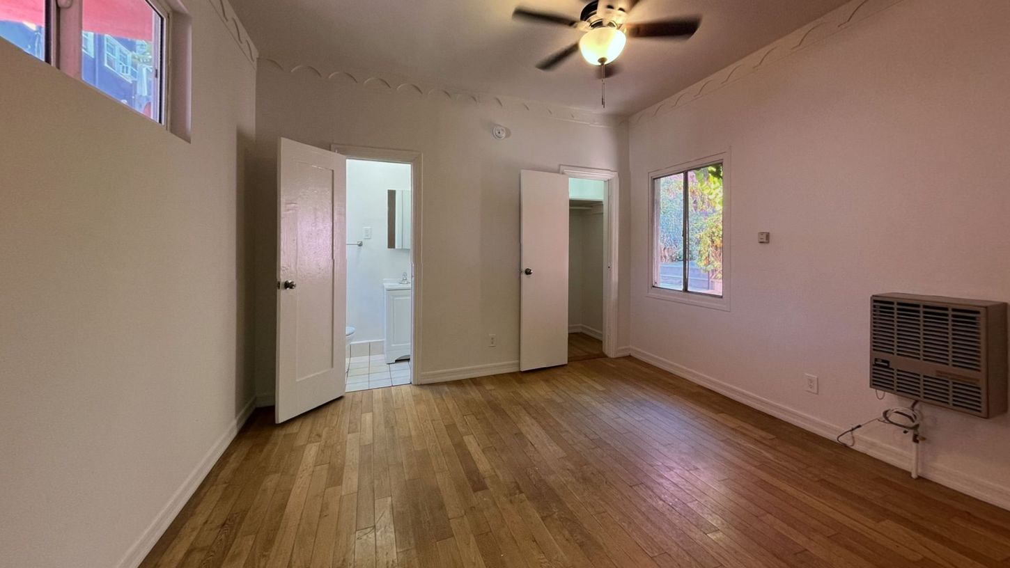 Empty room with hardwood floors, two windows, and an open doorway to a bathroom.