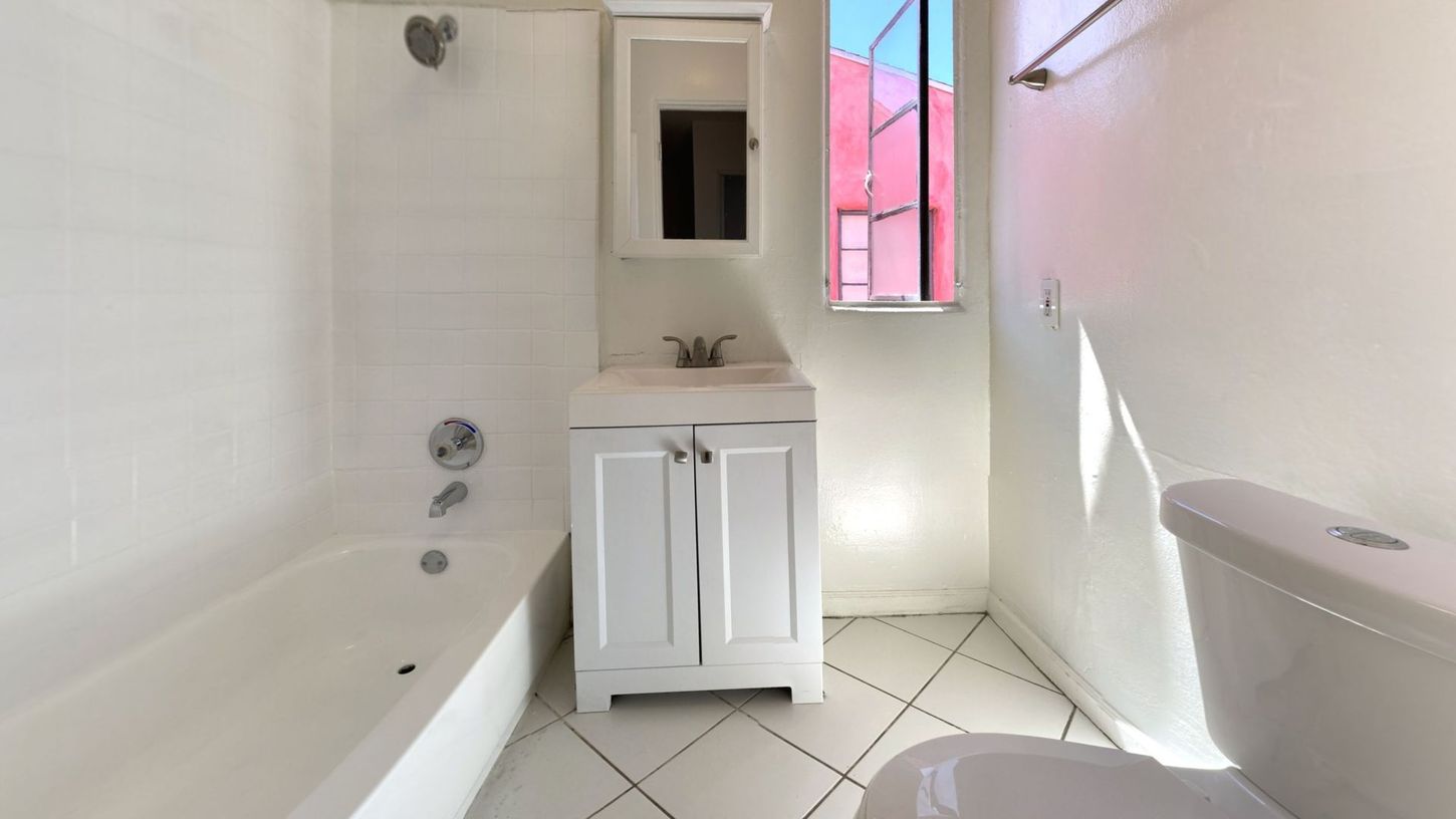 White bathroom with a bathtub, sink, toilet, and window.
