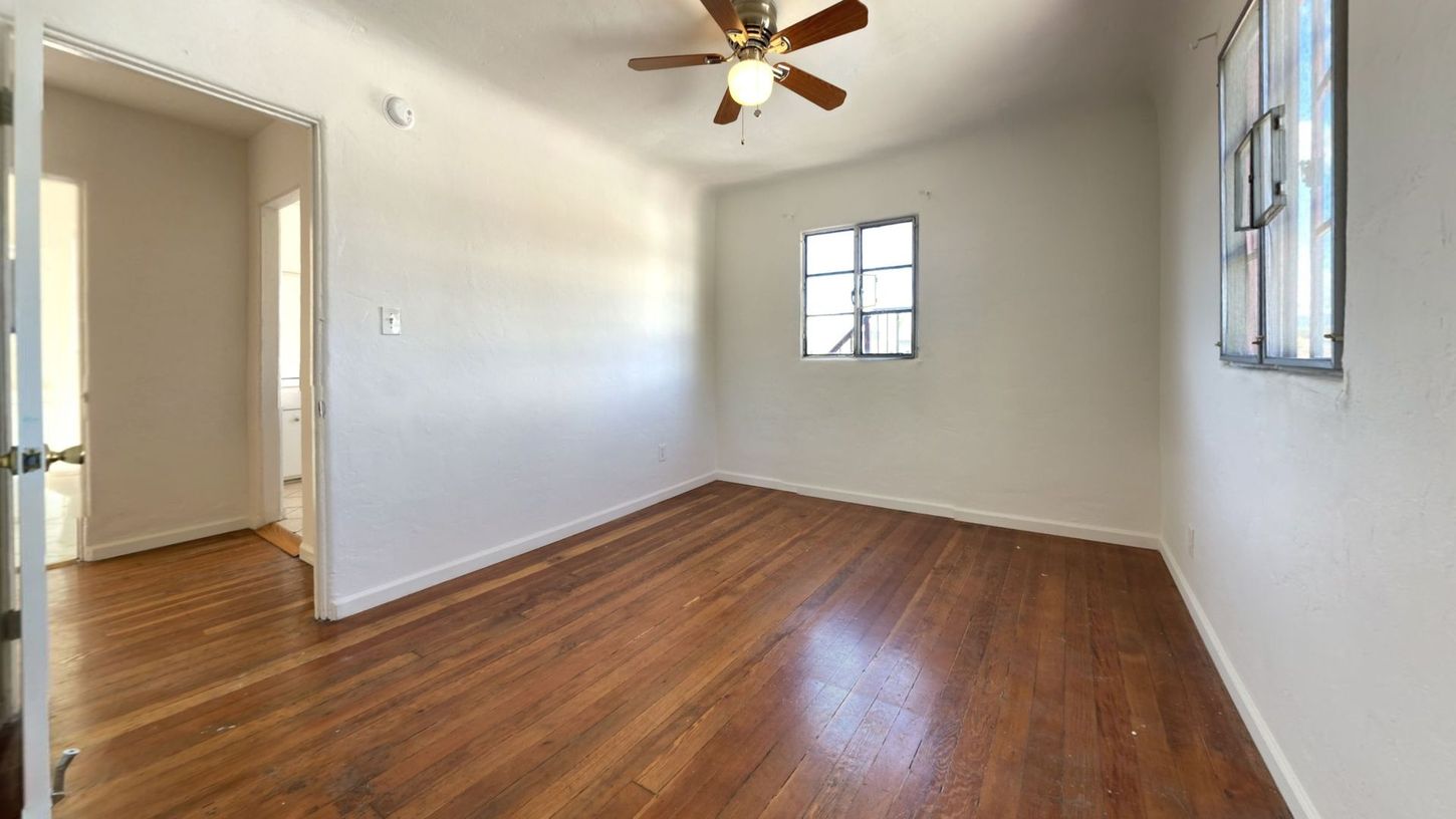 Empty room with hardwood floors, white walls, and a ceiling fan.