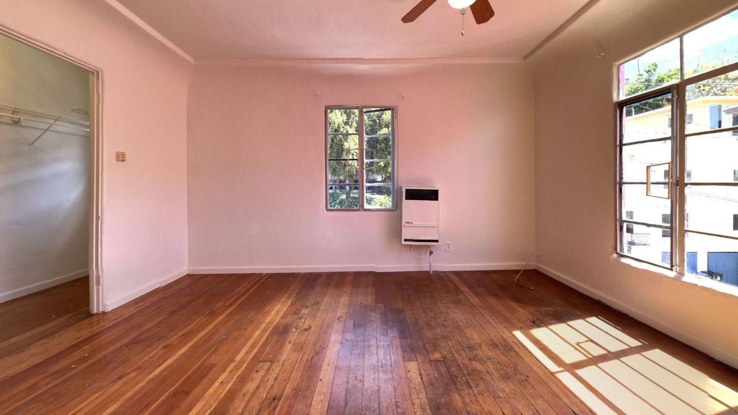 Empty room with hardwood floors, two windows, and a wall heater.