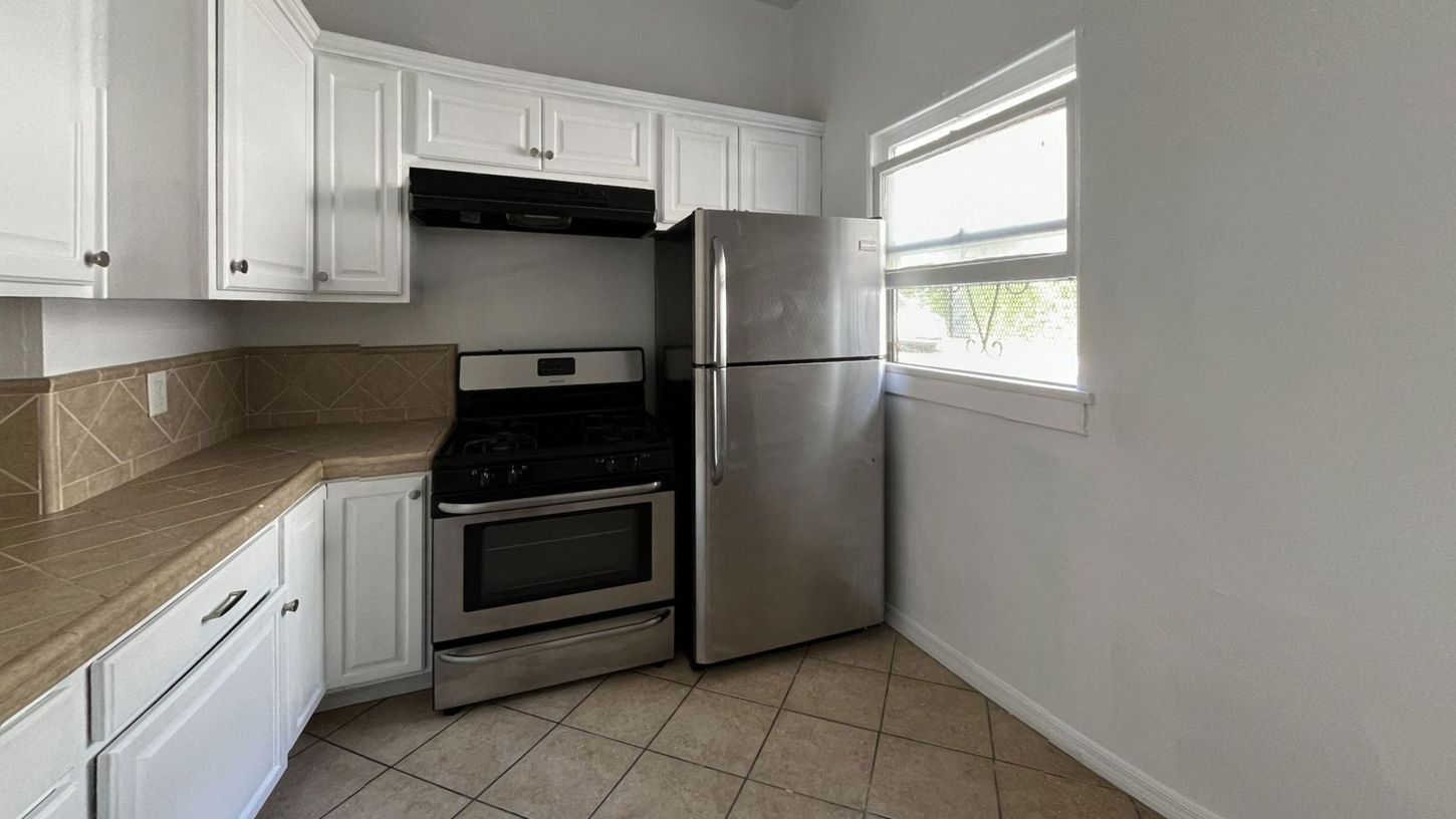 Kitchen with white cabinets, stainless steel appliances, tile flooring, and a window.