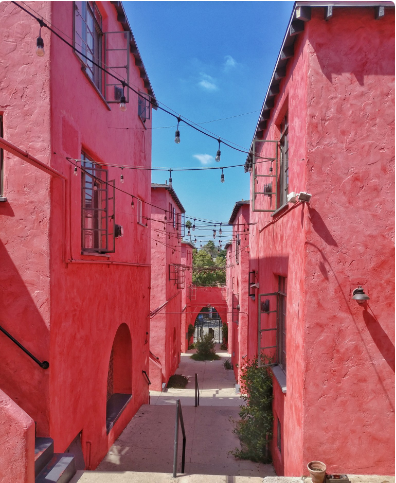 Red buildings with string lights over a walkway; blue sky visible.