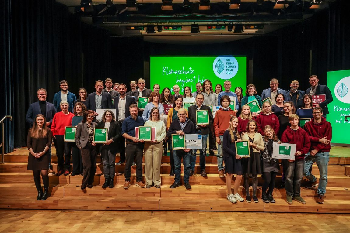 Eine große Gruppe von Menschen posiert auf einer Bühne für ein Foto.