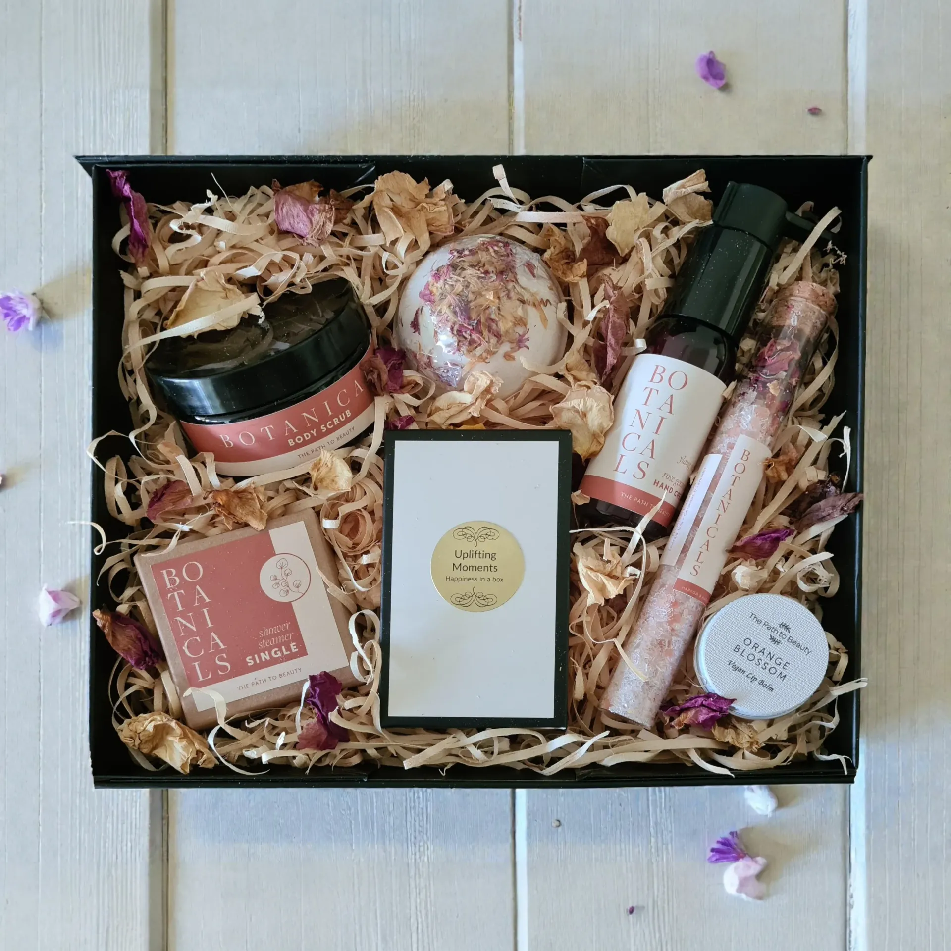 Gift box with beauty products on wood shavings; includes a jar, bath bomb, roller bottle, lip gloss, and soap.