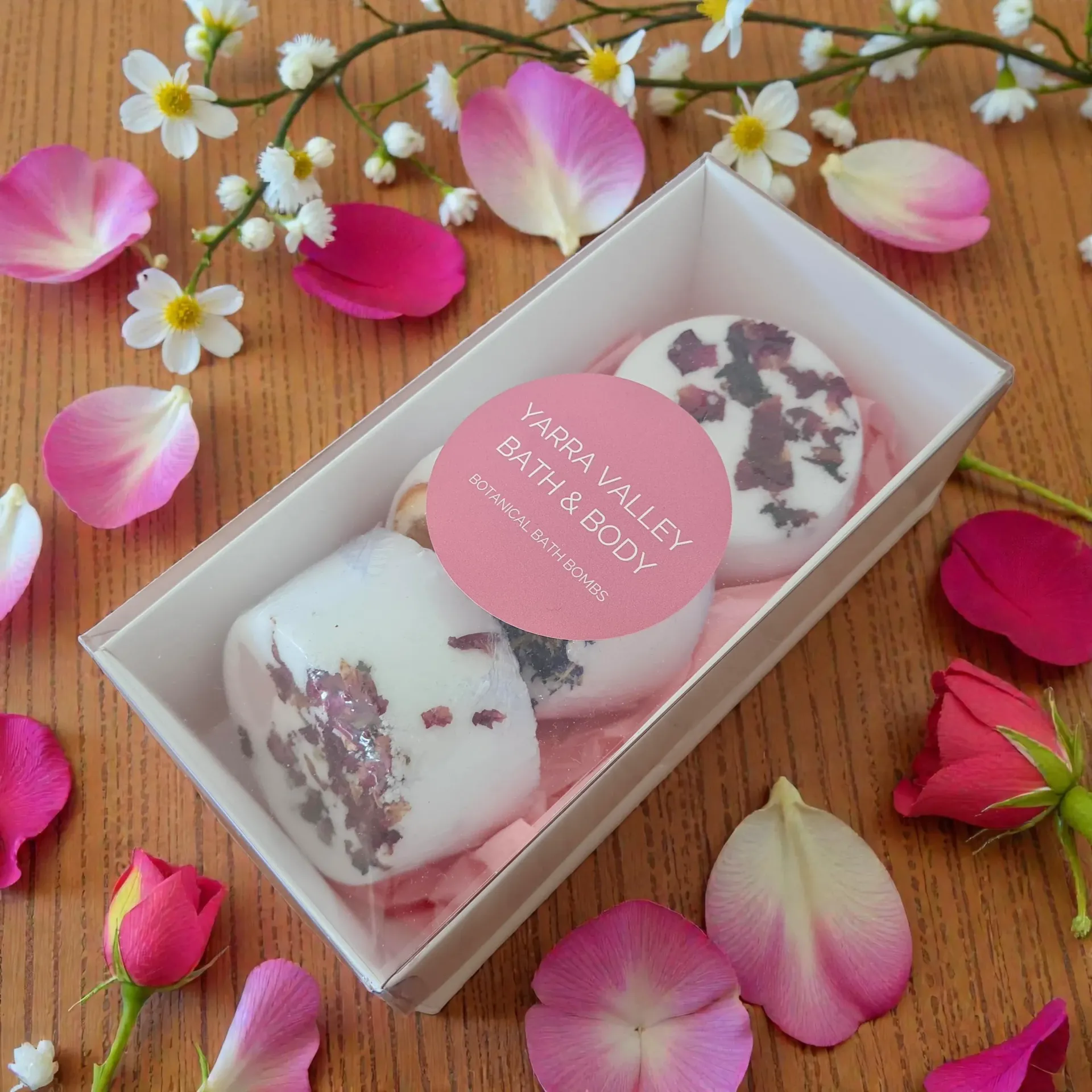 Bath bombs in a box, surrounded by rose petals and flowers.