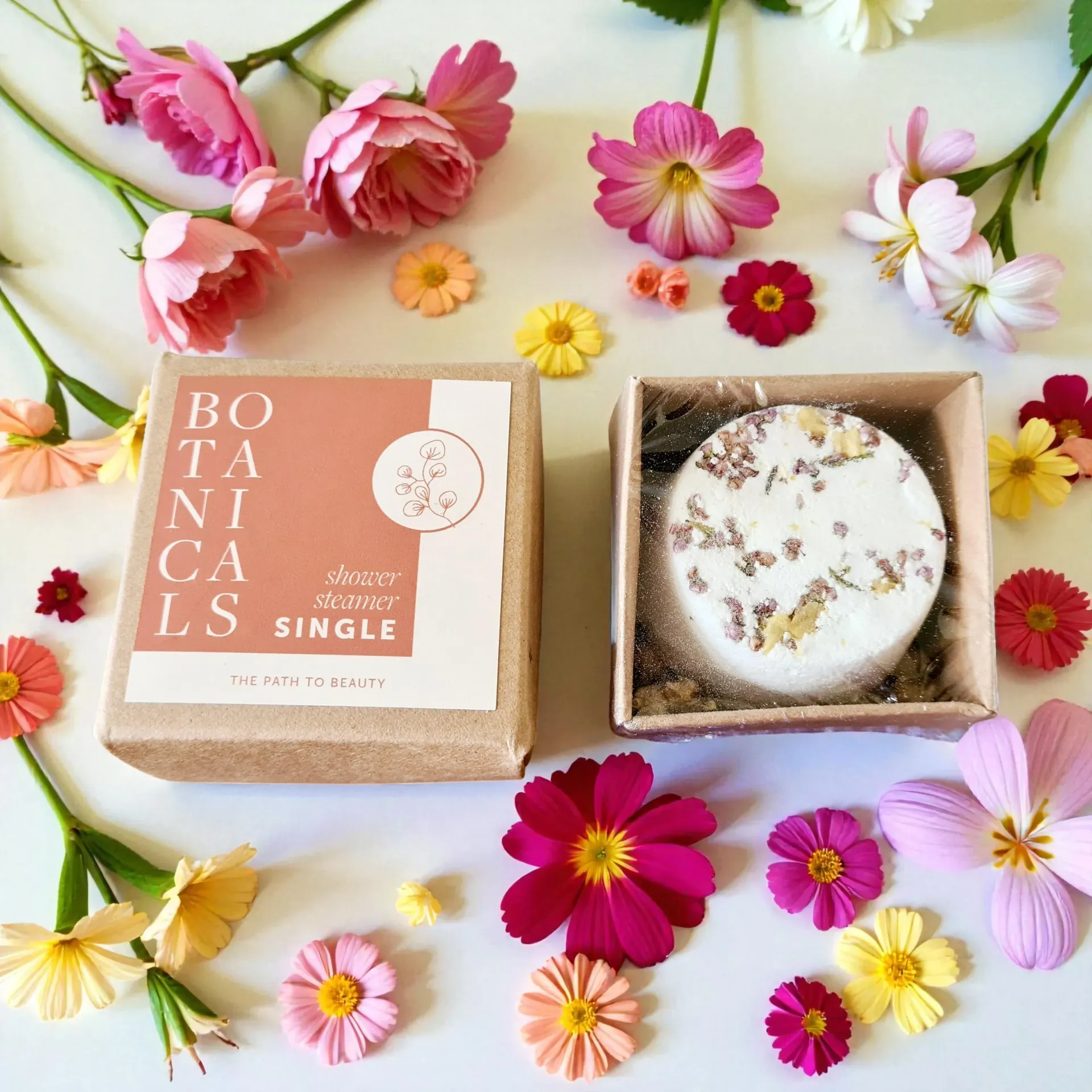 Open box with a botanical shower steamer, surrounded by colorful flowers.