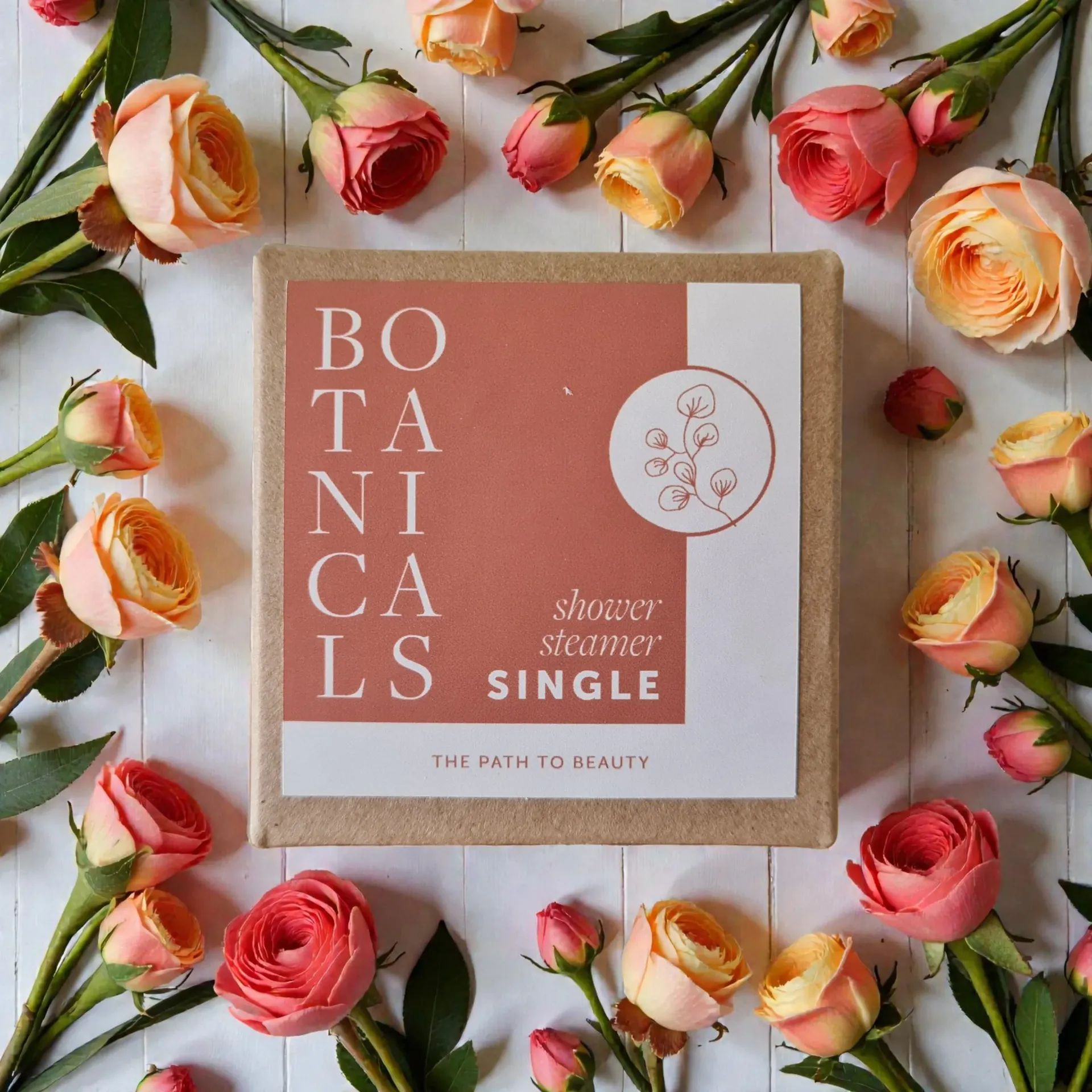 Open box with a botanical shower steamer, surrounded by colorful flowers.
