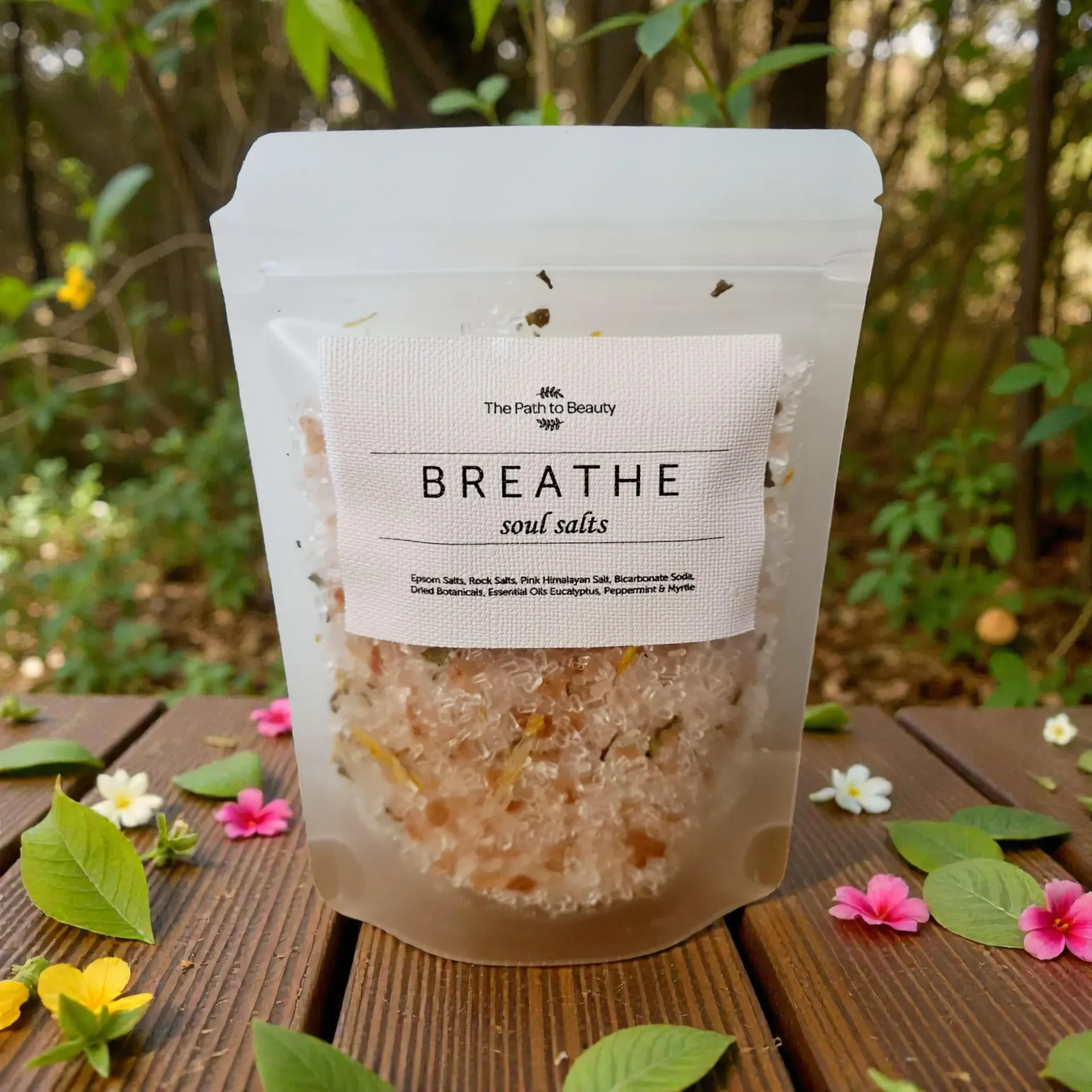 Breathe bath salts in a clear pouch with label on a wooden surface surrounded by leaves and flowers.
